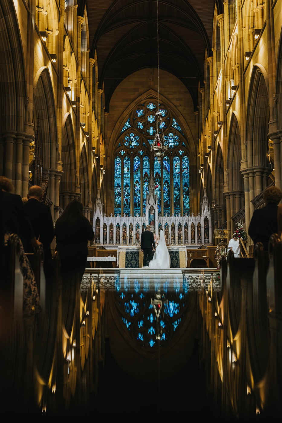 Couple kneeling at the altar of St Mary's Cathedral, the stained glass reflected in the aisle