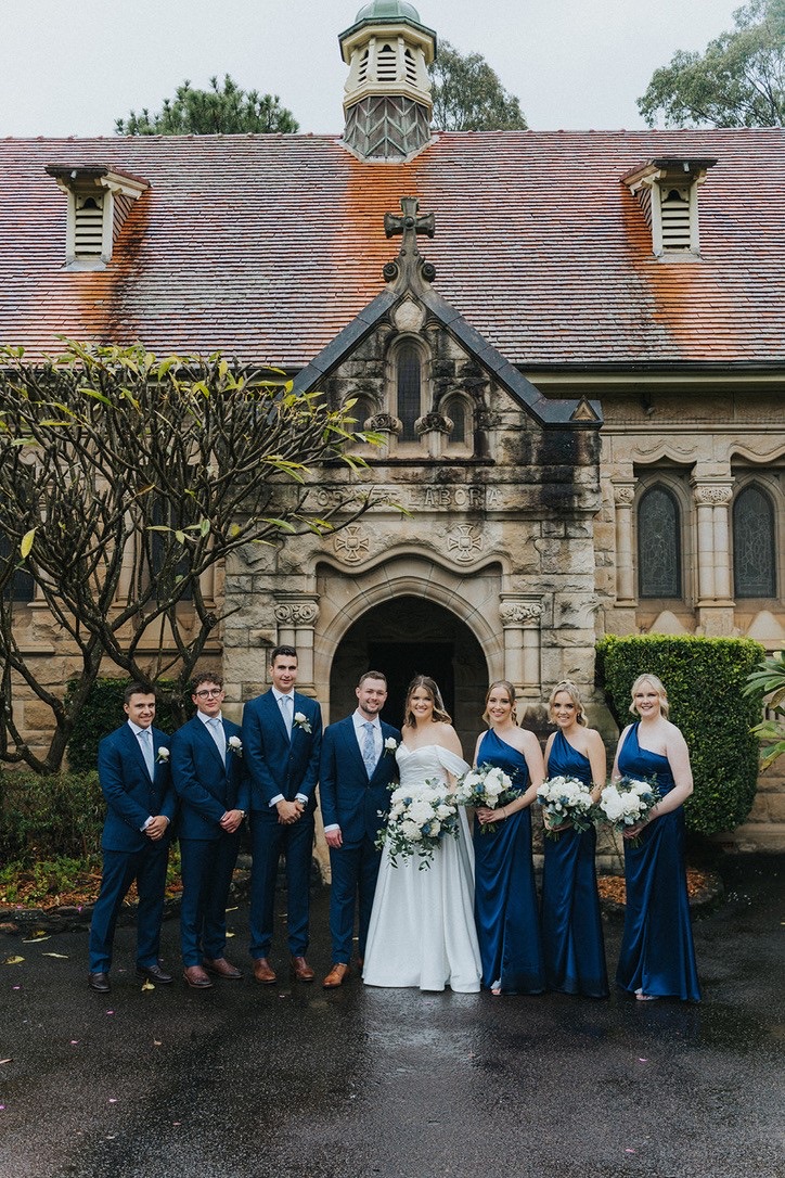 Bridal party in navy outside a sandstone chapel