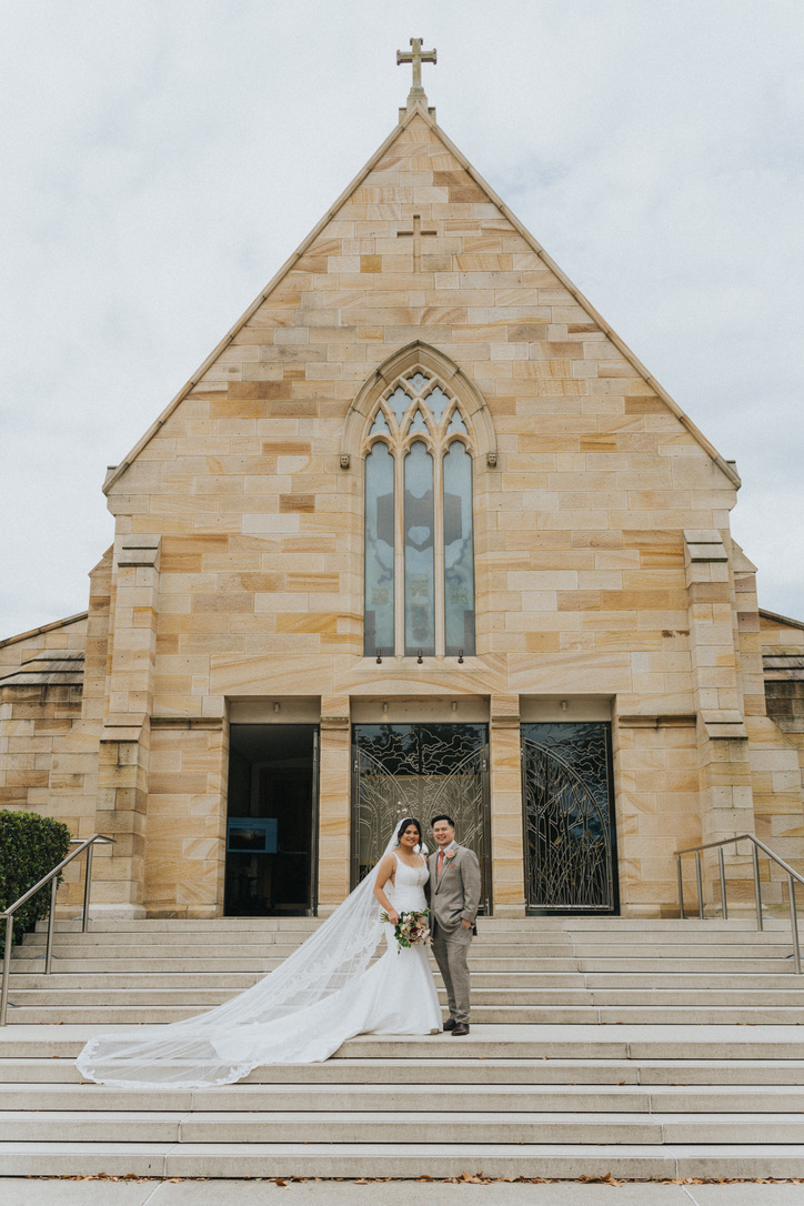 Couple on the steps of a sandstone church beneath the cross