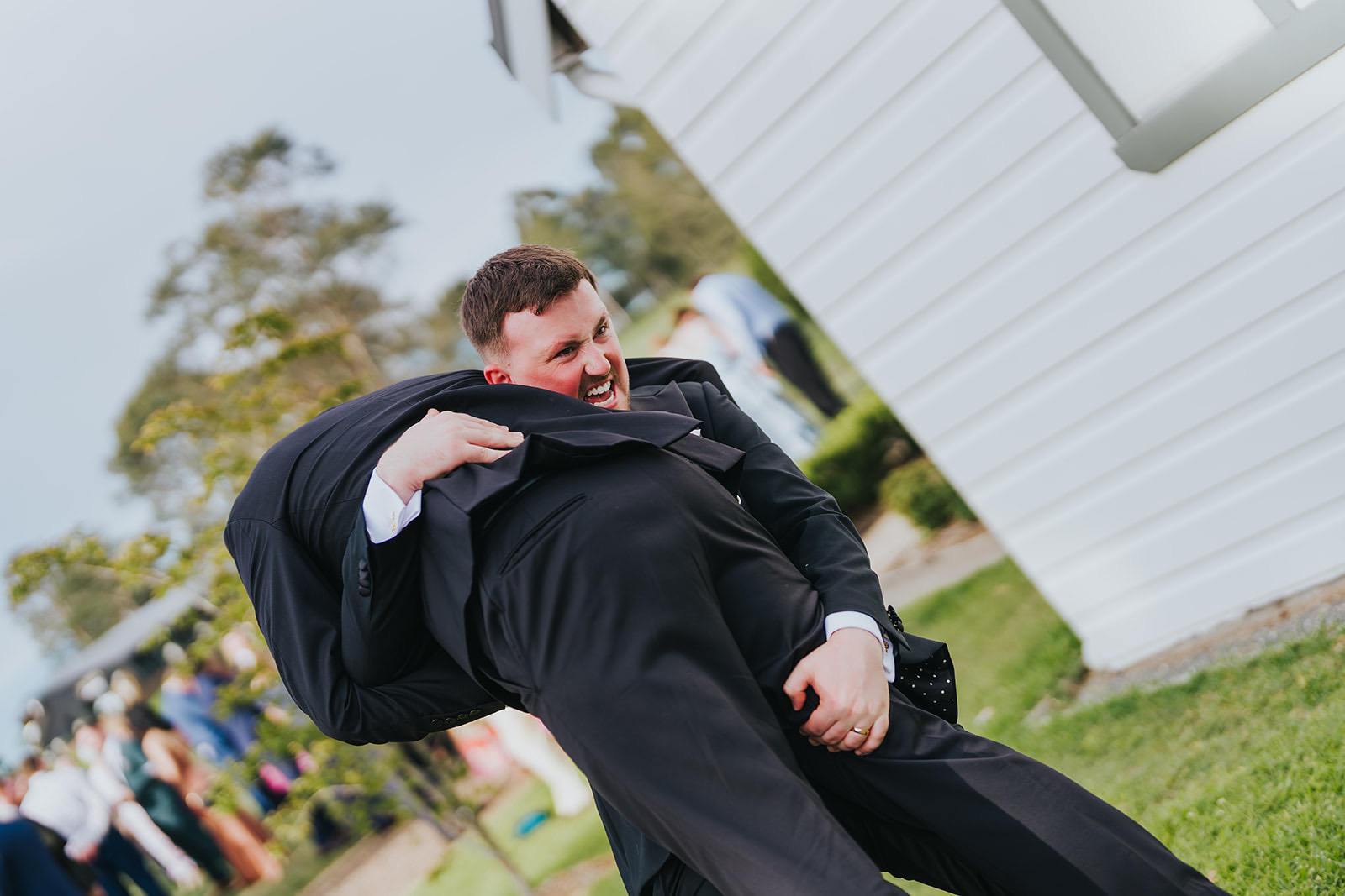 Groomsmen lifting Lachlan in front of the chapel