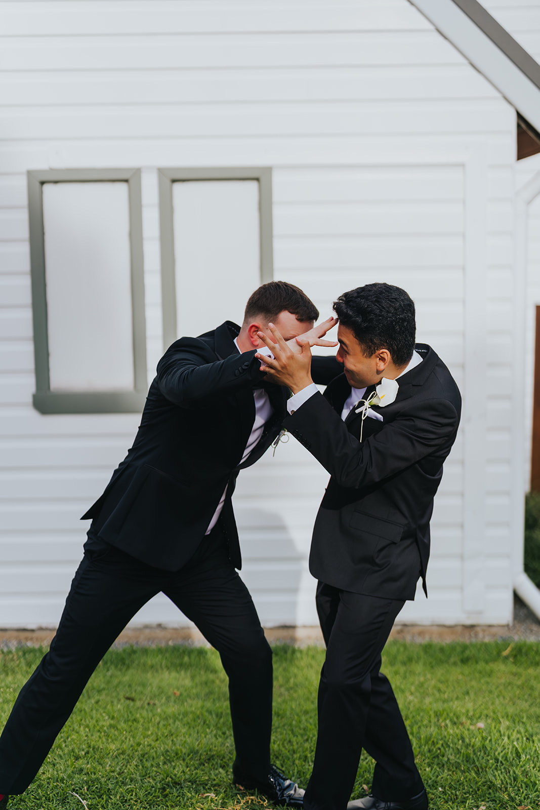 Two groomsmen play-fighting on the lawn
