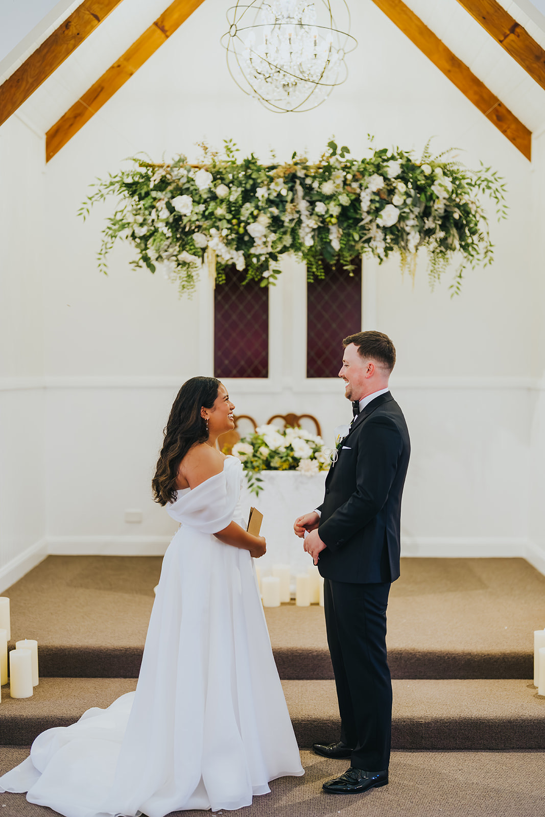 The couple facing each other beneath the greenery at the chapel altar