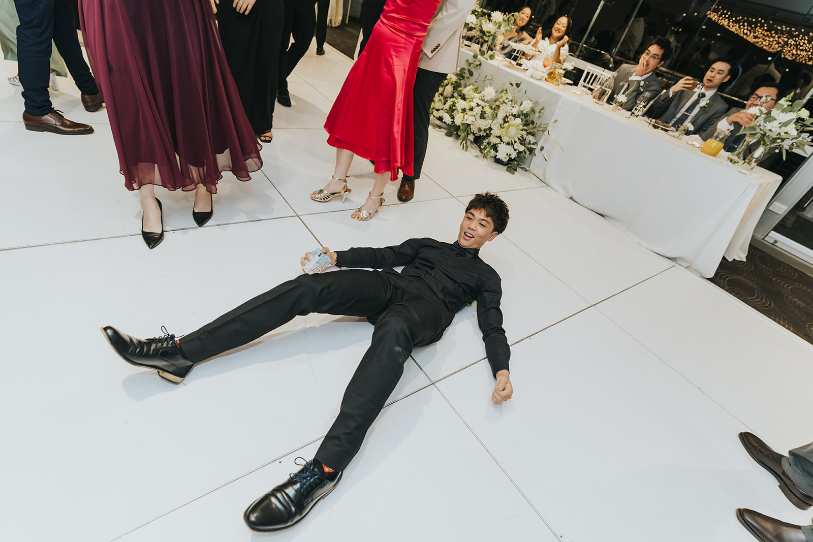 A groomsman lying on the dance floor as guests laugh