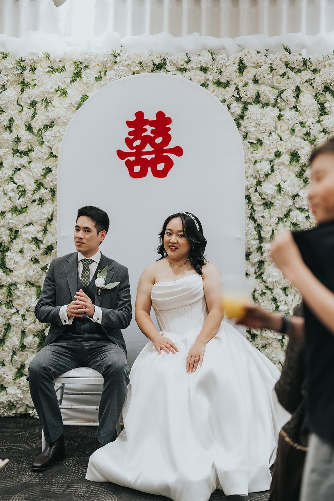 Jimmy and Cathy seated in front of a white flower wall for their tea ceremony