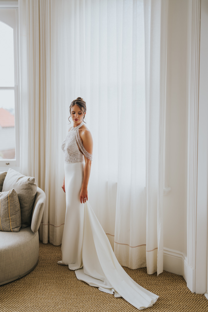 Bride standing by sheer curtains in soft window light